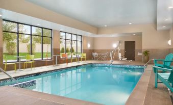 an indoor swimming pool with a blue water surface , surrounded by glass windows and chairs at Home2 Suites by Hilton Joliet/Plainfield