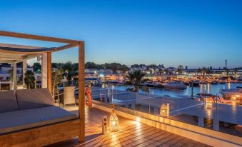 a wooden deck with a bed on it , overlooking a harbor filled with boats at dusk at Lago Resort Menorca Casas del Lago