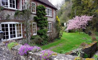 a brick house surrounded by a lush green lawn , with trees and flowers in the background at Bridge Cottage