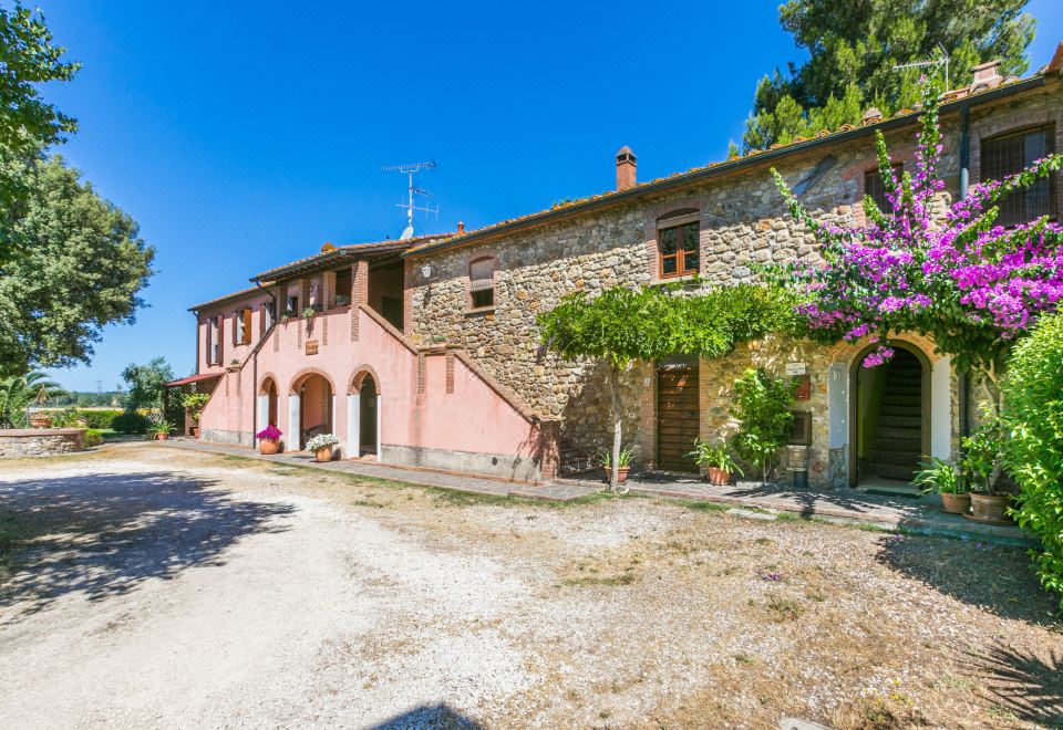 a beautiful stone house with a red door , surrounded by lush greenery and flowers , under a clear blue sky at Marrone