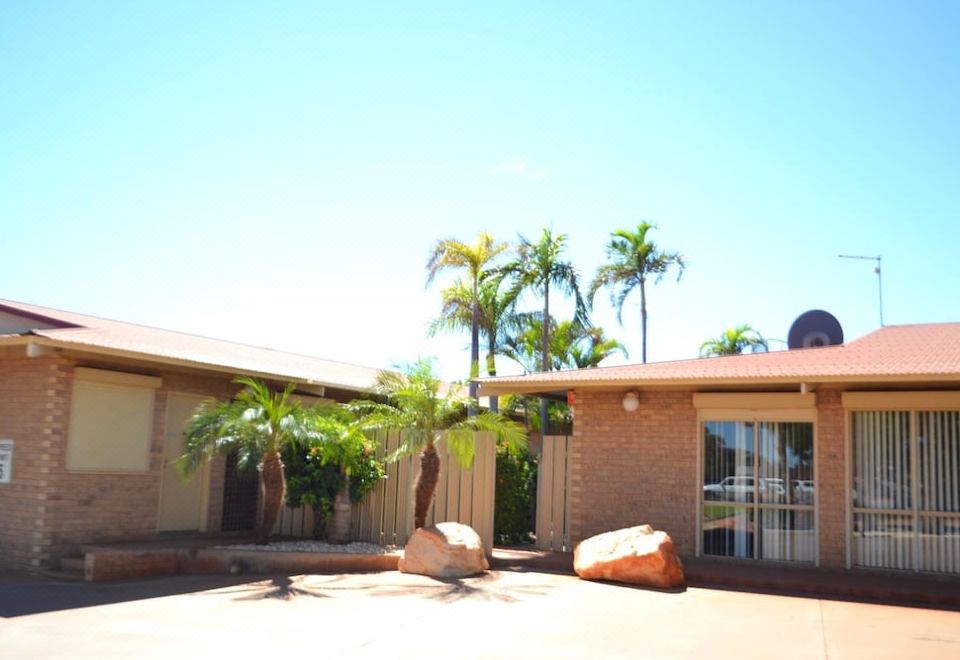 a brick house surrounded by palm trees , with a large rock in front of it at The Lodge Motel