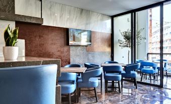 a modern restaurant with blue chairs and tables , a tv on the wall , and large windows at The District Hotel