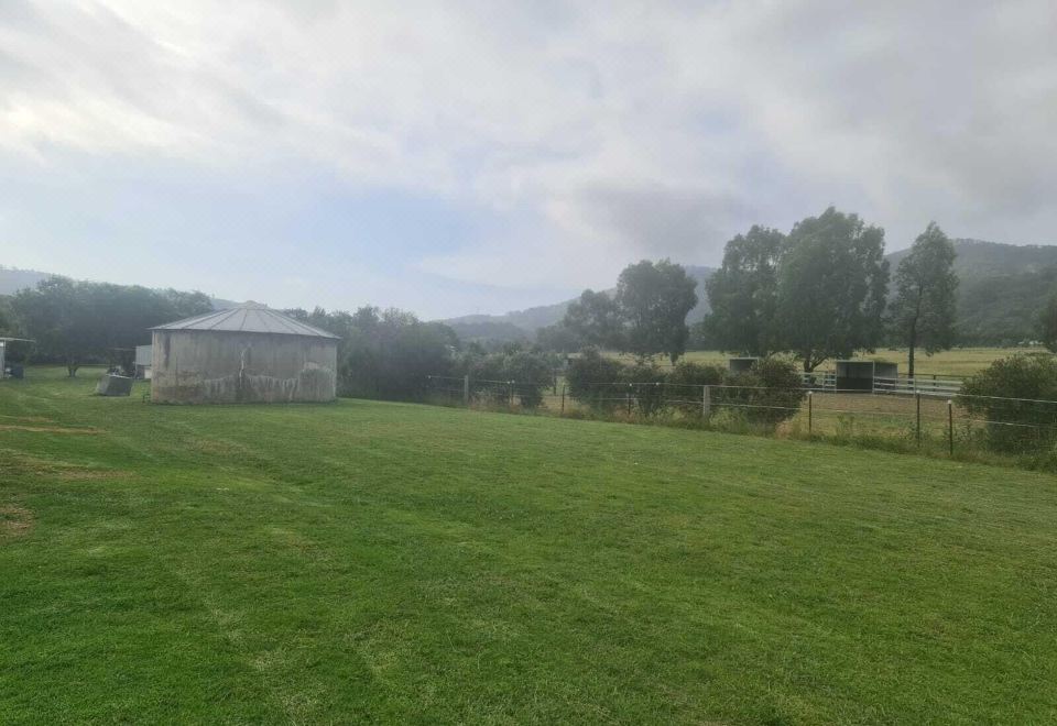 a grassy field with a barn in the background , under a cloudy sky and surrounded by trees at Valley View Motel