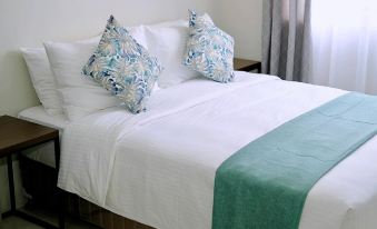 a neatly made bed with white sheets and blue and green pillows , accompanied by a green comforter at Sukro