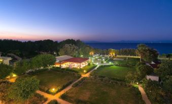 a large , well - maintained garden with a building and grassy area in the center of a field at dusk at Bayside Hotel Katsaras