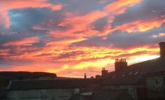 a beautiful sunset over a city , with a person standing on a rooftop looking up at the sky at Fife Arms Hotel