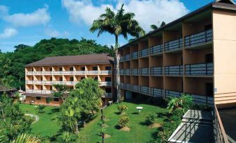 a large , multi - story building with a tropical setting and lush greenery surrounding it , including palm trees and other plants at Grafton Beach Resort