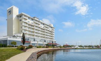 a large white hotel building situated next to a body of water , with a pier extending into the water at The Inn at Harbor Shores