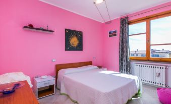 a pink bedroom with a white bed , a window , and a tv . also a bathroom visible in the room at Mansarda