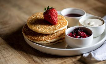 a white plate with three pancakes topped with strawberries , accompanied by a bowl of berries and a cup of milk at The Exeter Inn