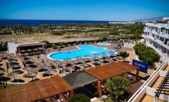 a resort with a large pool surrounded by lounge chairs , umbrellas , and a beach in the background at Ohtels Cabogata