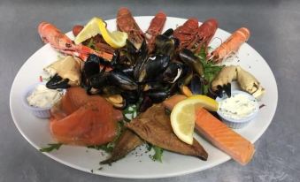 a large platter filled with a variety of seafood , including lobster , shrimp , and salmon , sits on a dining table at Loch Shiel Hotel