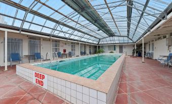 "a large indoor swimming pool with a "" deep end "" sign on the side , surrounded by chairs and tables" at Bayside Hotel