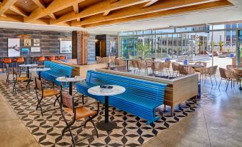 a modern restaurant with wooden tables , blue benches , and large windows , providing a view of the outdoors at Hotel Indigo El Paso Downtown