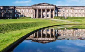 a large , stone building with columns and a reflection of the building in the water at Hampton by Hilton  Edinburgh Airport