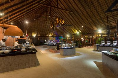 a large room with a high ceiling and thatched roof has a buffet table filled with various food items at Vilamendhoo Island Resort & Spa