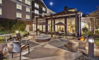 an outdoor dining area with a fire pit and chairs , surrounded by a building with a large window at Hilton Garden Inn Akron-Canton Airport