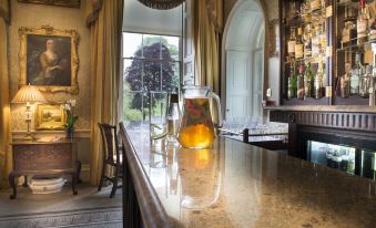 a bar area with a large window , gold curtains , and various bottles and glasses on the counter at Ston Easton Park