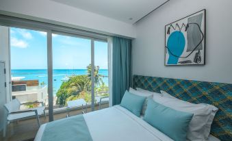 a bedroom with a large window overlooking the ocean , featuring a bed with blue pillows and a painting of a blue bird at Ocean V Hotel