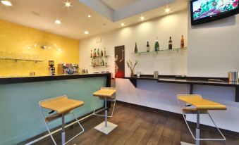 a modern bar area with two stools and a tv mounted on the wall , along with various bottles and cups at Best Western Cesena Hotel