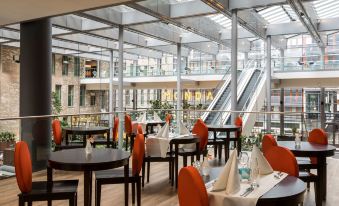 an indoor restaurant with wooden tables and chairs , white tablecloths , and an open glass ceiling at NH Den Haag