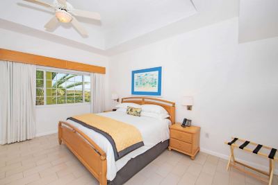 a cozy bedroom with a wooden bed , white walls , and a ceiling fan , under a blue painting at Wyndham Reef Resort Grand Cayman