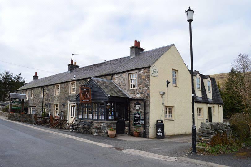 a stone building with a black awning and a large window is on the street corner at Cross Keys