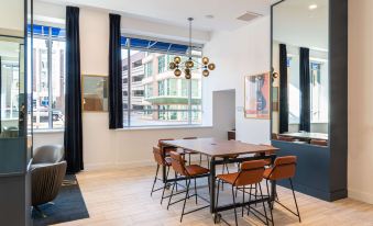 a modern dining room with a large table and chairs , surrounded by windows and a high ceiling at Hilton Garden Inn Flint Downtown