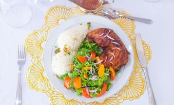 a plate of food on a dining table , consisting of chicken , rice , and vegetables at Royal Elmount Hotel