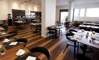 a restaurant with wooden floors and tables , black chairs , and white plates is shown at Tulip Inn Itaguai