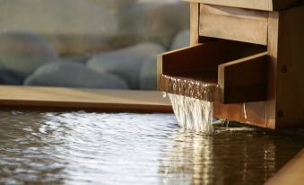 a waterfall of water flowing from a wooden door into a pool of water in a room at La Vista Hakodate Bay