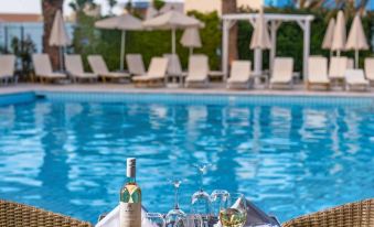 a table set up for a meal with wine glasses and plates of food near a pool at Minos Boutique Hotel