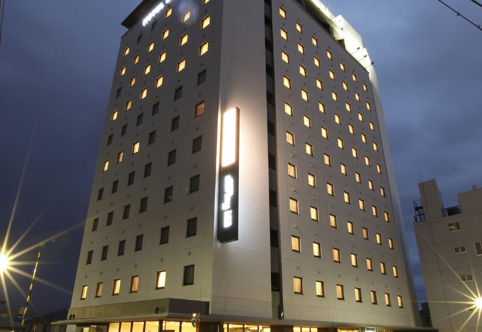 a tall white building with many windows and a sign on the side , illuminated at night at Dormy Inn Mishima
