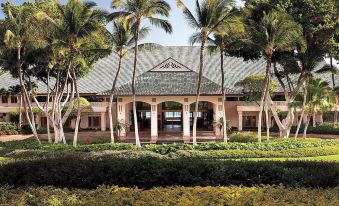 a large building with palm trees surrounding it , creating a serene and tropical atmosphere in the background at Four Seasons Resort Lana'i