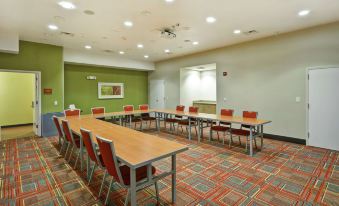 a conference room with a long table surrounded by red chairs and green walls at Home2 Suites by Hilton Rochester Henrietta