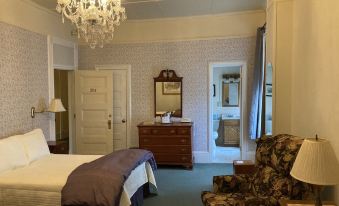 a bedroom with a bed , dresser , and chair is shown with a chandelier hanging above at The Brandon Inn