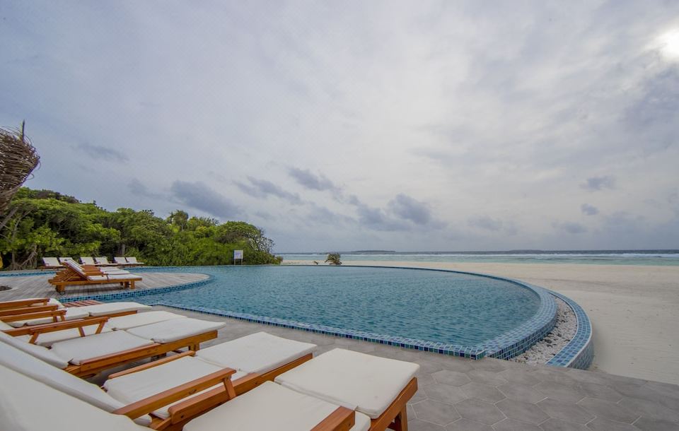 a large , circular swimming pool surrounded by lounge chairs on a deck overlooking the ocean at Hondaafushi Island Resort