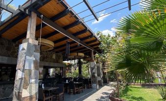 a covered outdoor dining area with stone pillars , wooden tables , and chairs under a wooden roof , surrounded by lush greenery at Las Jaras Aguas Termales
