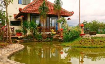 a beautiful house with a red tile roof is surrounded by lush greenery and a pond at De View Hotel