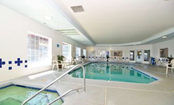 an indoor swimming pool with a diving board , surrounded by chairs and benches for seating at Lighthouse Suites Inn