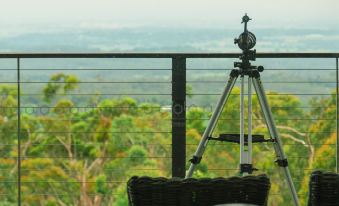 a tripod is set up on a balcony overlooking a green forest and mountains , with black chairs and cushions arranged around it at Spicers Sangoma Retreat