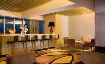 a modern bar with a bartender behind the counter , surrounded by chairs and tables in a hotel lobby at Novotel Bangka - Hotel & Convention Centre