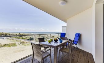 a wooden deck with a table and chairs set up for outdoor dining , overlooking the ocean at Balnea