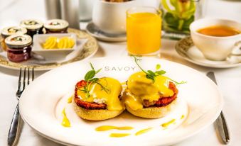 a white plate with two pastries topped with hollandaise sauce and a glass of orange juice , sitting on a table at The Savoy Hotel