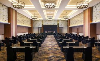 a large conference room with rows of tables and chairs , a stage , and chandeliers hanging from the ceiling at Royal Ambarrukmo Yogyakarta