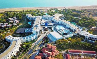 aerial view of a large hotel surrounded by trees , with a body of water in the background at Lykia World Antalya - All Inclusive