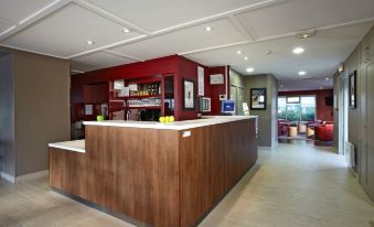 a modern , well - lit restaurant with a wooden counter and red walls , along with several chairs and tables at Campanile Rouen Est - Franqueville Saint Pierre