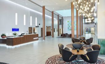 a modern hotel lobby with white walls , wooden columns , and a reception desk , as well as several chairs arranged around it at Hilton Garden Inn Sunderland