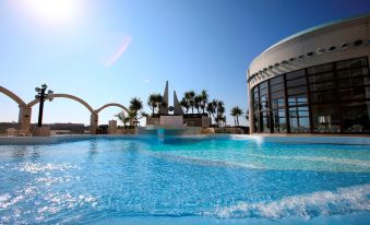 a large swimming pool with a curved roof and palm trees in the background , under a clear blue sky at Loisir Hotel Naha