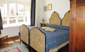 a bedroom with a large bed and a window , featuring two blue bedspreads and gold - framed pictures on the wall at Villa Margherita